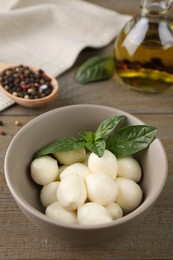 Photo of Tasty mozarella balls and basil leaves in bowl on wooden table