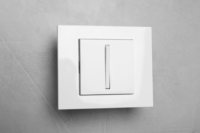 Photo of White light switch on grey background, closeup