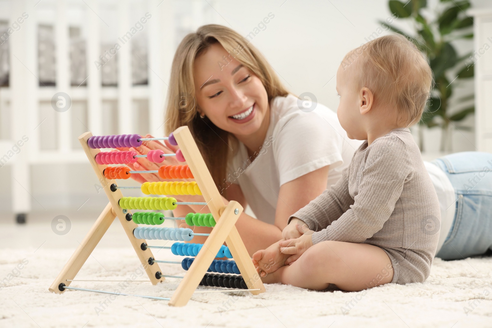 Photo of Children toys. Happy mother and her little son playing with wooden abacus on rug at home