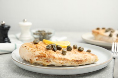 Photo of Delicious chicken fillet with capers and lemon served on light grey table, closeup