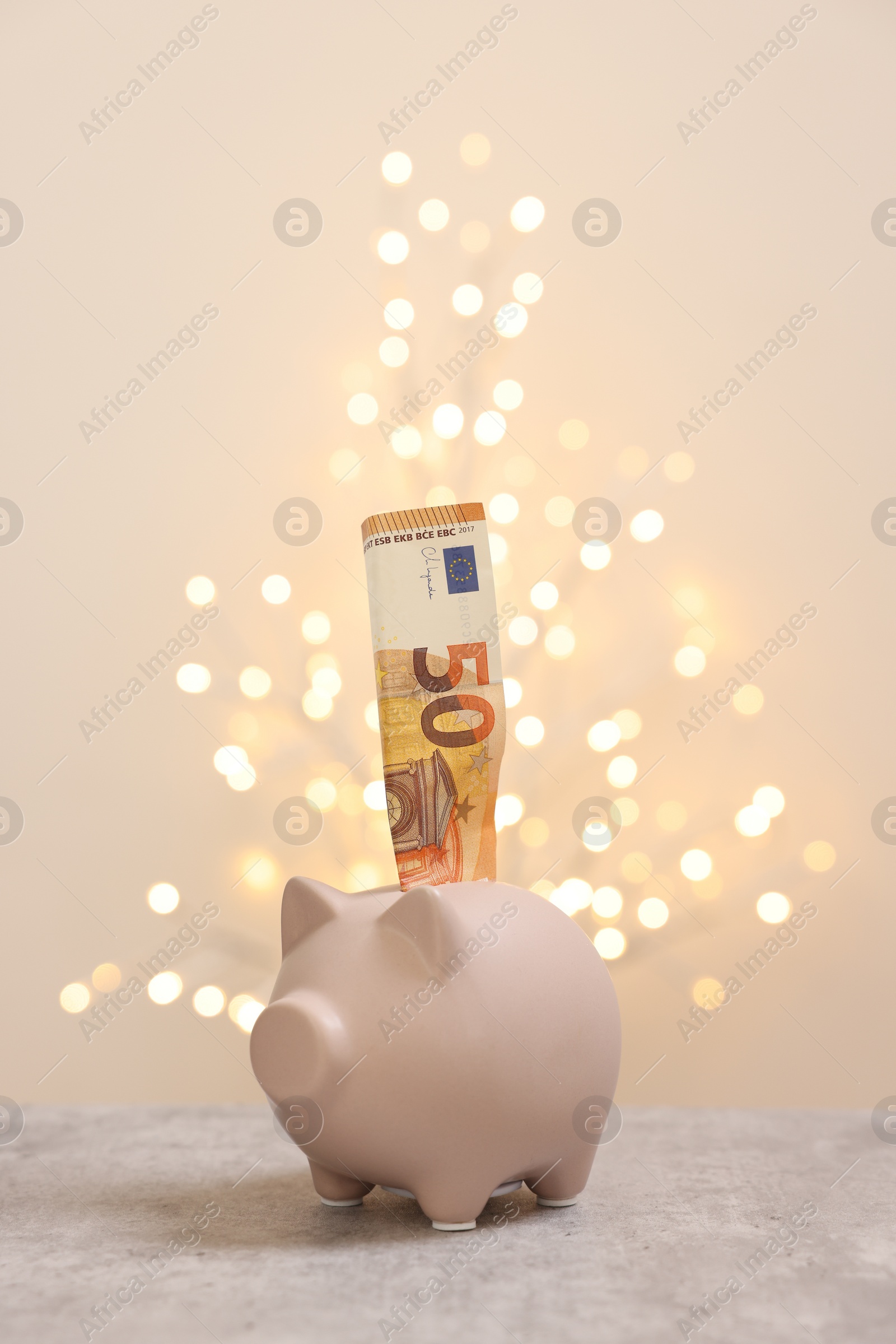 Photo of Piggy bank with euro banknote on grey table against blurred lights