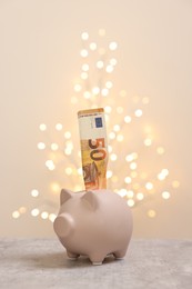 Piggy bank with euro banknote on grey table against blurred lights