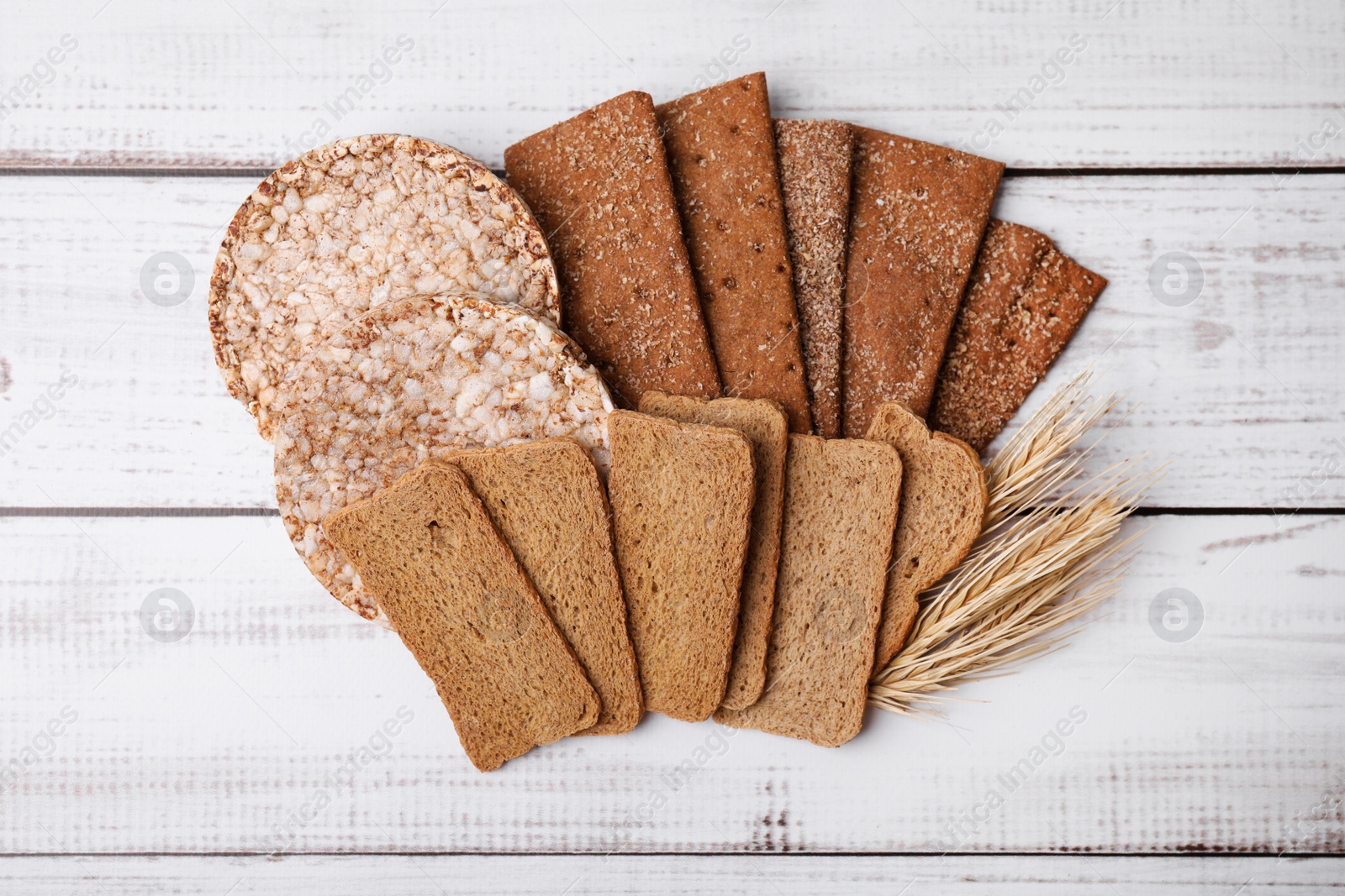 Photo of Rye crispbreads, rice cakes and rusks on white wooden table, flat lay