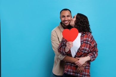 Lovely couple with red paper heart on light blue background, space for text. Valentine's day celebration