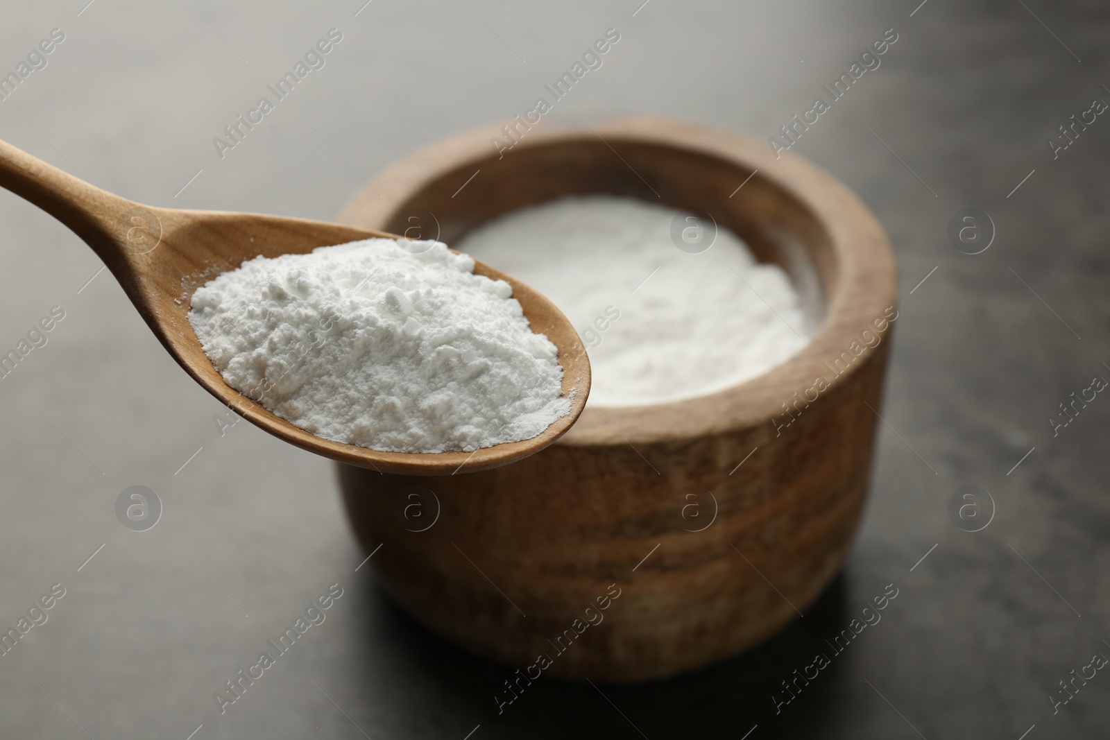 Photo of Spoon of baking powder over bowl at grey textured table, closeup. Space for text