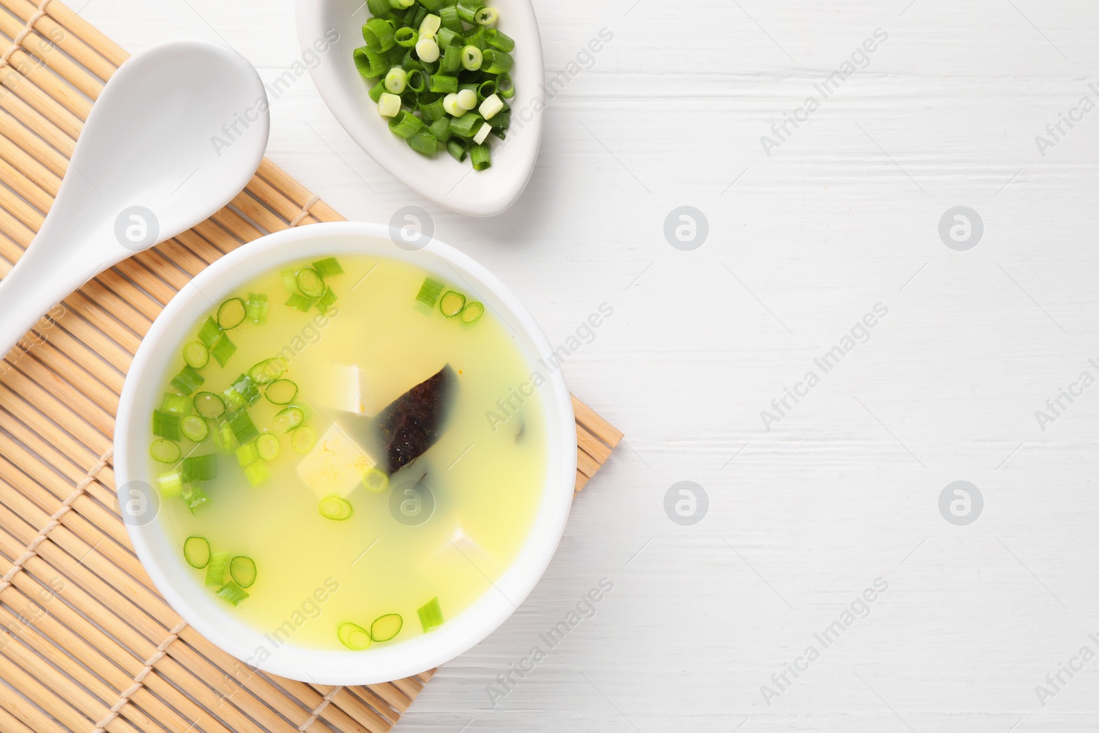 Photo of Bowl of delicious miso soup with tofu served on white wooden table, flat lay. Space for text