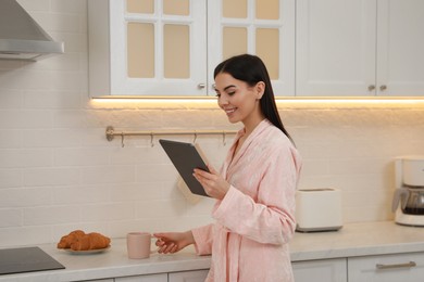 Photo of Young woman with tablet having breakfast in kitchen. Morning routine