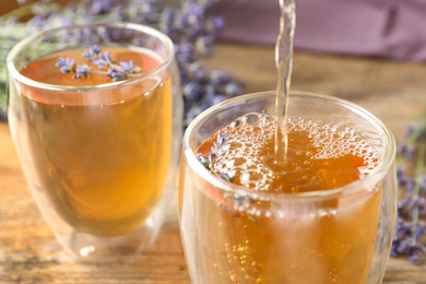 Photo of Pouring delicious lavender tea into glass, closeup