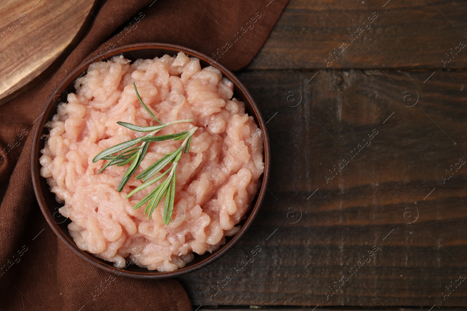 Photo of Fresh raw minced meat and rosemary in bowl on wooden table, top view. Space for text