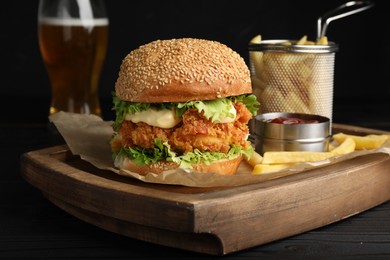 Photo of Delicious burger with crispy chicken patty, french fries, sauce and beer on black wooden table