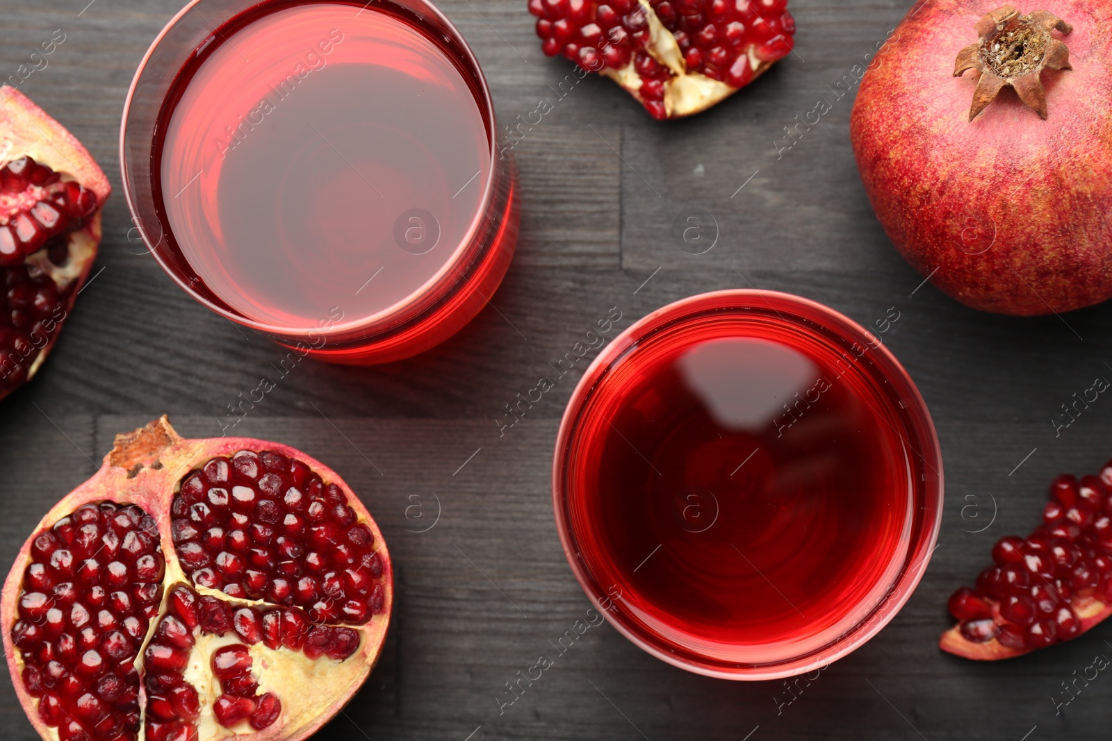 Photo of Tasty pomegranate juice in glasses and fresh fruits on black wooden table, flat lay