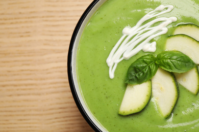 Photo of Tasty homemade zucchini cream soup on wooden table, top view