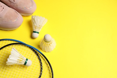 Photo of Feather badminton shuttlecocks, rackets and sneakers on yellow background, above view. Space for text
