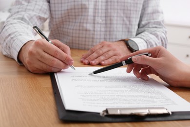 Photo of Businesspeople signing contract at wooden table, closeup of hands