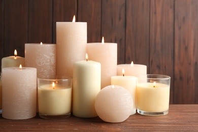 Photo of Set of burning candles on table against wooden background