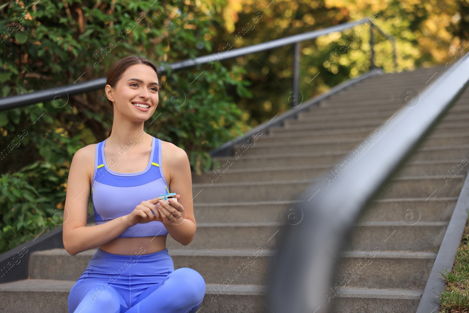 Photo of Attractive happy woman checking pulse with blood pressure monitor after training on stairs in park. Space for text