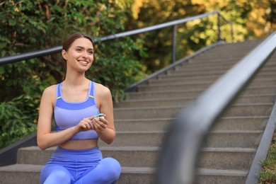 Attractive happy woman checking pulse with blood pressure monitor after training on stairs in park. Space for text