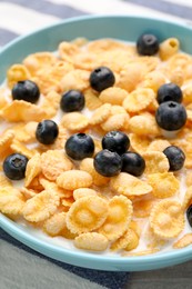 Photo of Bowl of tasty crispy corn flakes with milk and blueberries on table, closeup