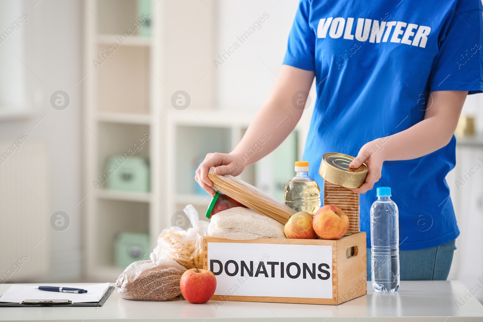 Photo of Female volunteer putting food products in donation box indoors