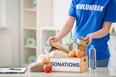 Female volunteer putting food products in donation box indoors