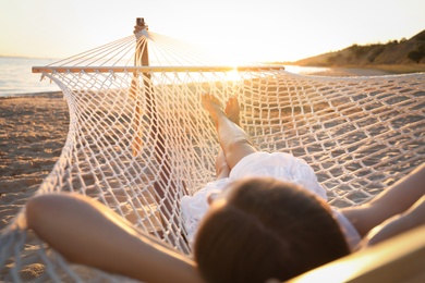 Photo of Young woman relaxing in hammock on beach at sunset, closeup