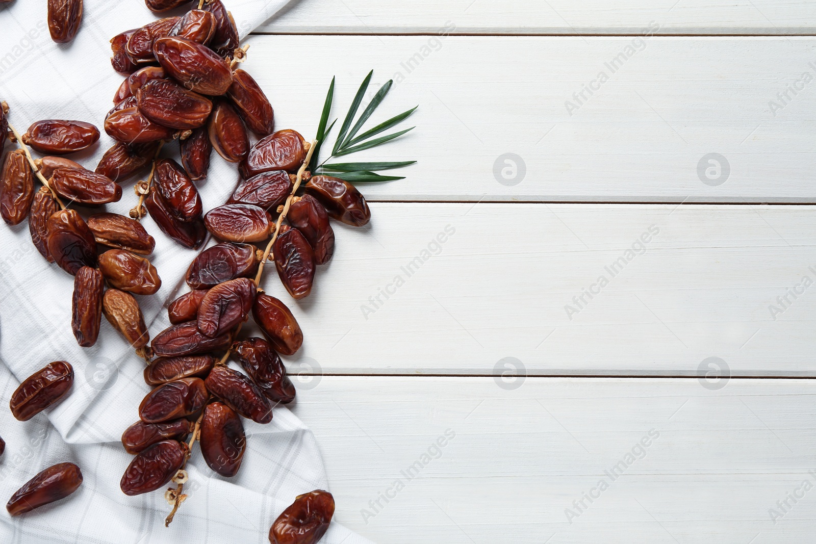 Photo of Tasty sweet dried dates and green leaf on white wooden table, flat lay. Space for text