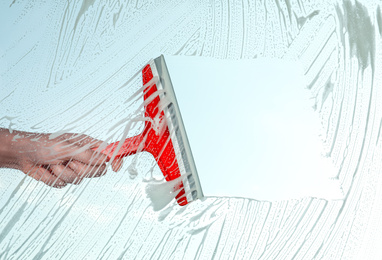 Photo of Woman cleaning window with squeegee on spring day, closeup