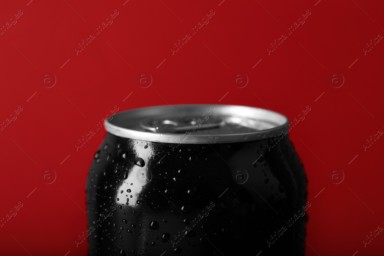 Photo of Black can of energy drink with water drops on red background, closeup