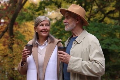 Photo of Affectionate senior couple with cups of coffee in autumn park