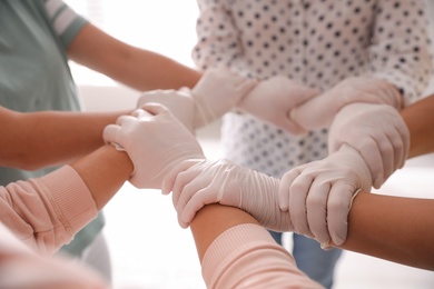 Photo of People in white medical gloves joining hands on light background, closeup