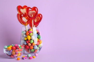 Photo of Delicious heart shaped lollipops and dragees on violet background. Space for text