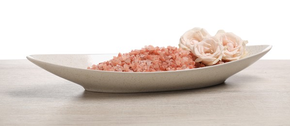 Photo of Natural sea salt in bowl and roses on light wooden table against white background