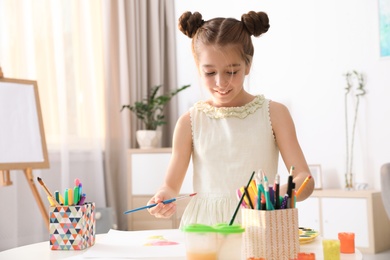 Photo of Little girl painting picture at table indoors