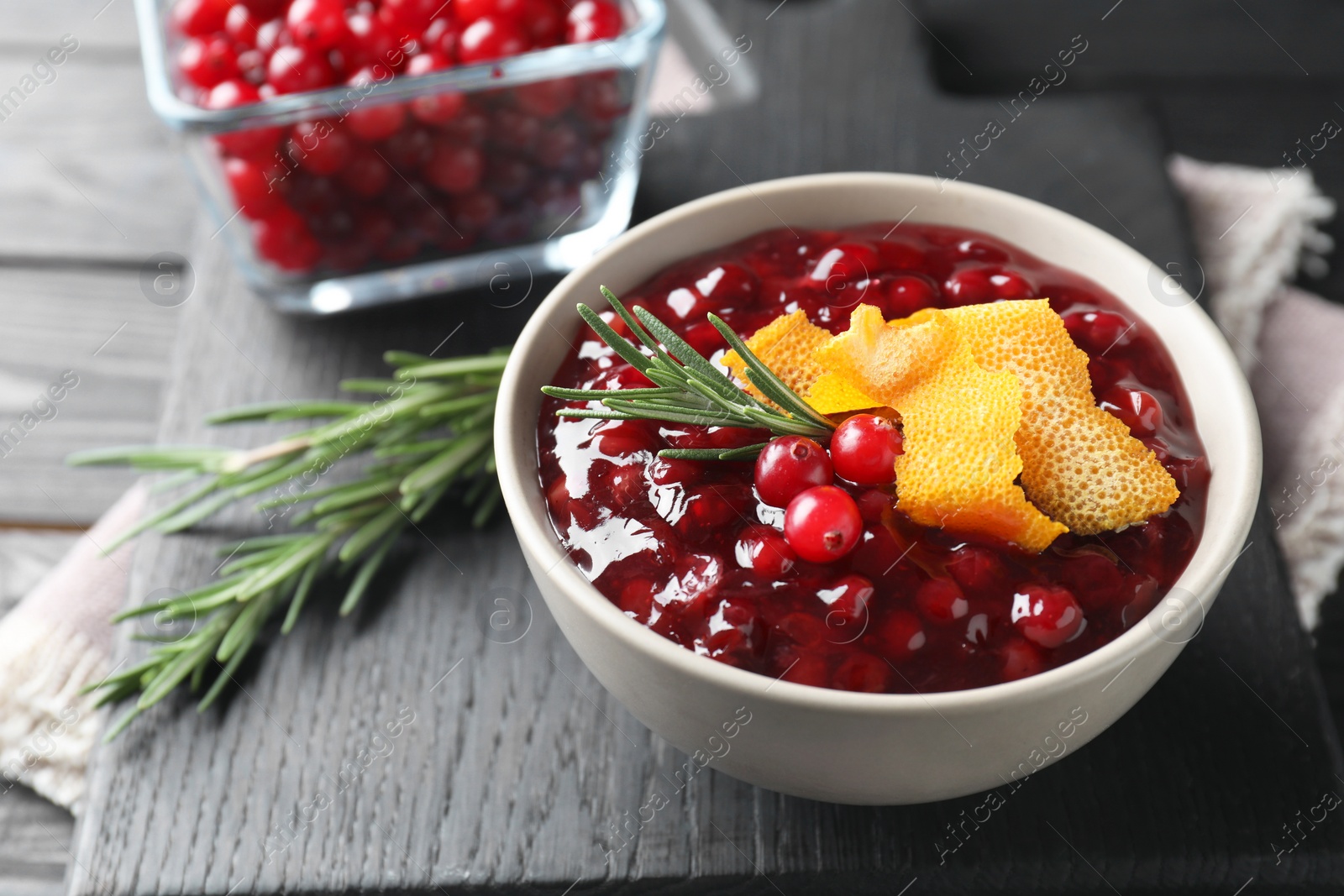 Photo of Fresh cranberry sauce, rosemary and orange peel in bowl on table, closeup