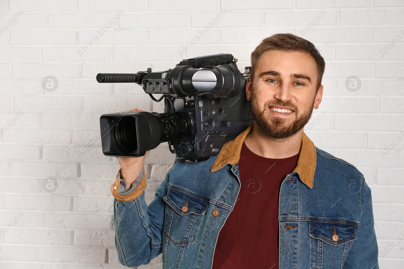 Photo of Operator with professional video camera near white brick wall