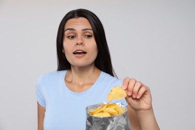 Beautiful woman eating potato chips on grey background
