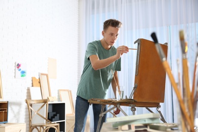 Teenage boy painting on easel in workshop, space for text. Hobby club