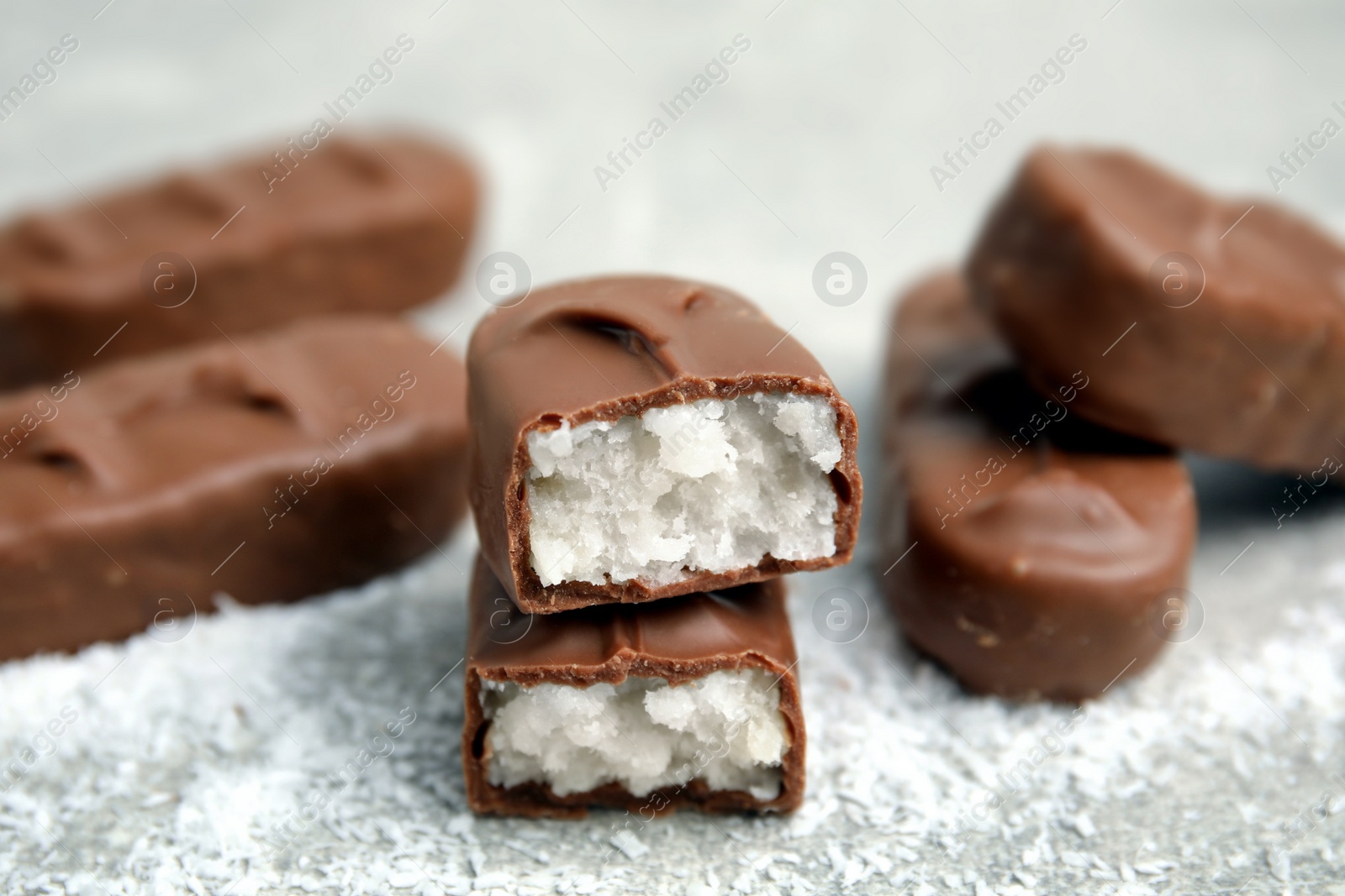 Photo of Delicious milk chocolate candy bars with coconut filling on grey table, closeup