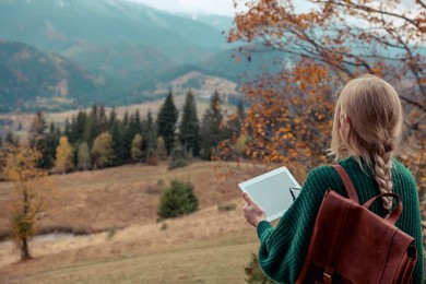 Young woman drawing on tablet in mountains, back view. Space for text