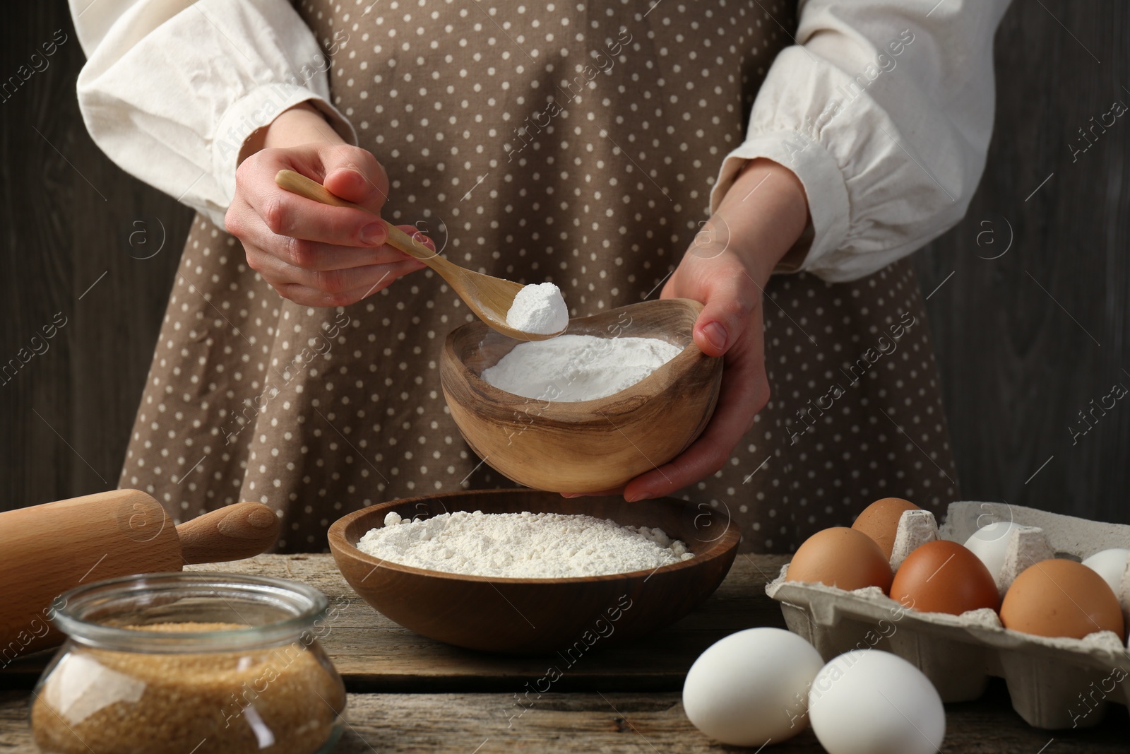 Photo of Making dough. Woman adding baking powder to flour at wooden table, closeup