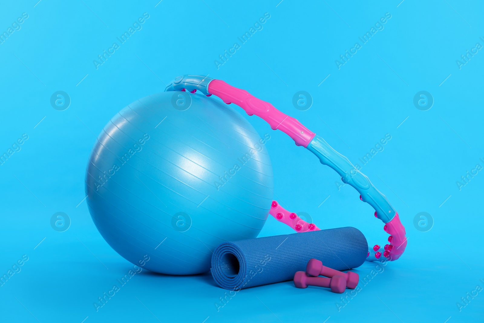 Photo of Hula hoop, exercise ball, yoga mat and dumbbells on light blue background