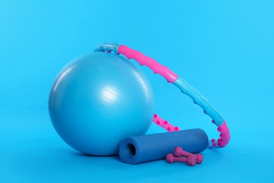 Hula hoop, exercise ball, yoga mat and dumbbells on light blue background