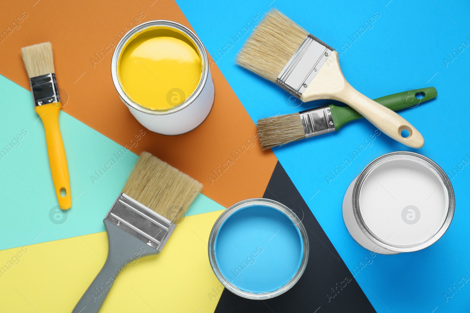 Photo of Cans of colorful paints and brushes on color background, flat lay