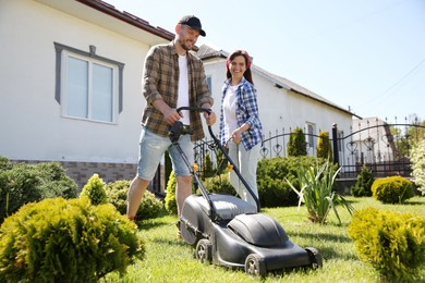 Happy couple spending time together while cutting green grass with lawn mower in garden