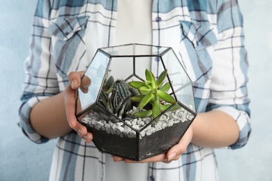 Young woman holding florarium with different succulents on color background, closeup