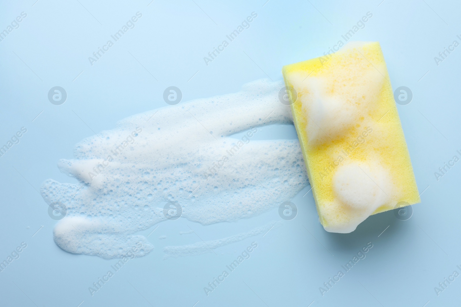 Photo of Yellow sponge with foam on light blue background, top view