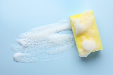 Yellow sponge with foam on light blue background, top view