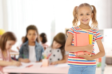 Image of Happy little girl with notebooks in classroom
