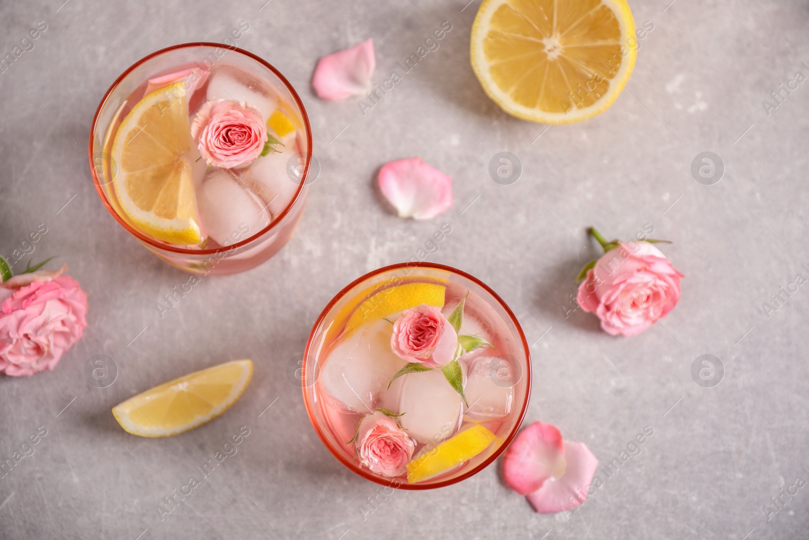 Photo of Tasty refreshing lemon drink with roses on light grey table, flat lay