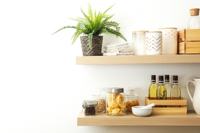 Photo of Wooden shelves with dishware and products on white wall. Kitchen interior idea